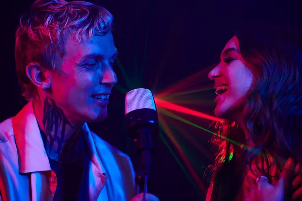 Un duo chante au karaoké box, micro en main, sous les néons